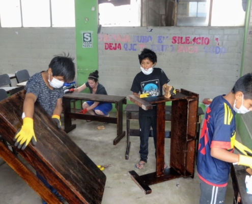 Volunteer repairing desks High School boys Sagrada Familia Peru
