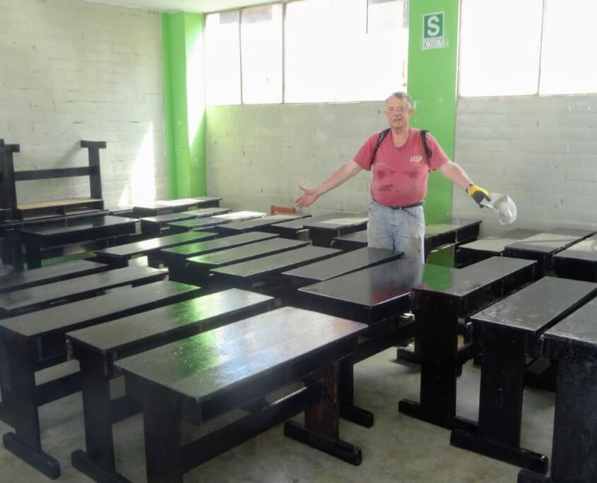 Volunteer proudly shows the refurbished desks at the Sagrada Familia high school in pERU
