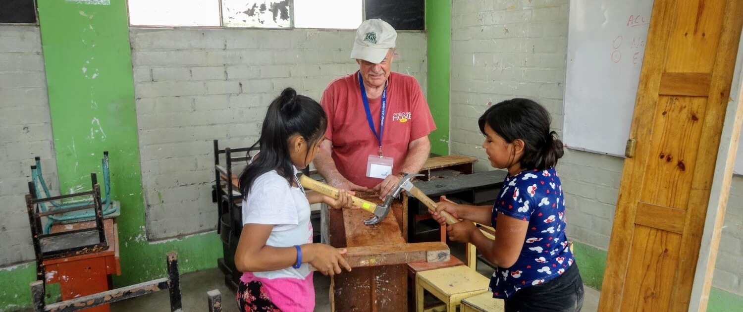 Volunteer Dave Horan repairs desks at the Sagrada Familia High School in Peru with local girls