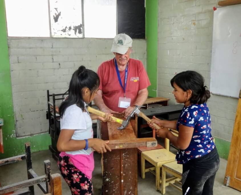 Volunteer Dave Horan repairs desks at the Sagrada Familia High School in Peru with local girls