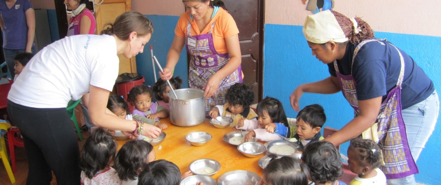 Volunteer helps feed children at an early childhood development center in Ecuador