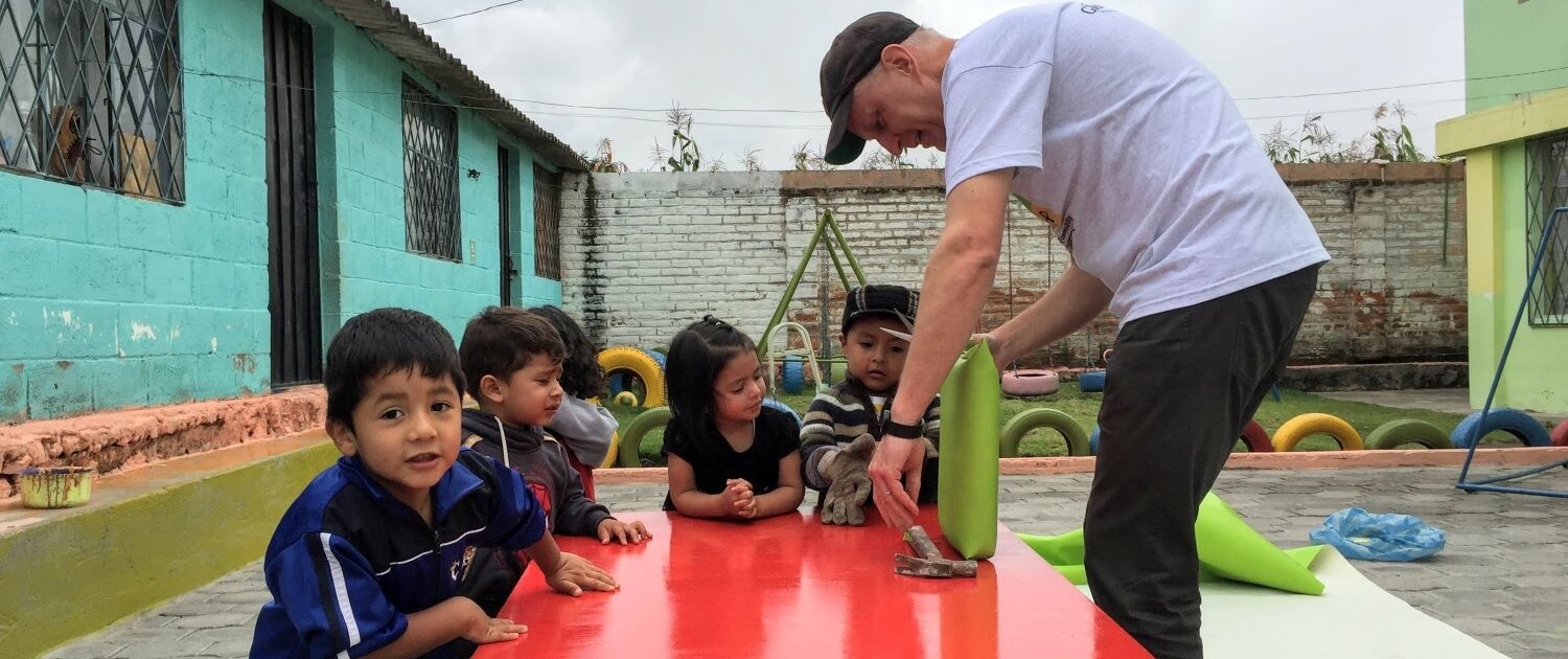 international Volunteer reupholsters seats while children watch an early childhood development center in Calderón, Ecuador.