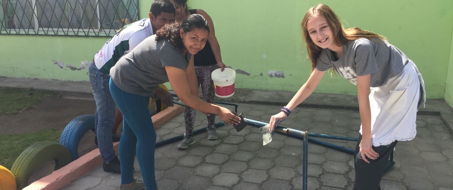 international Volunteer helps local moms sand and paint the playground at an early childhood development center in Calderón, Ecuador